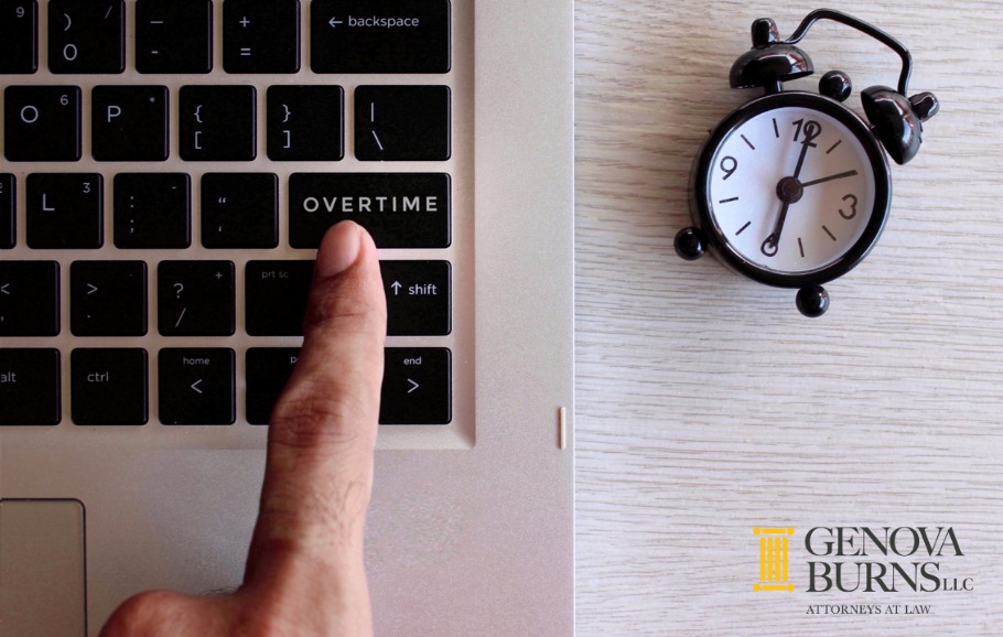 Finger pointing to an overtime button on a laptop keyboard that is on a desk with a clock